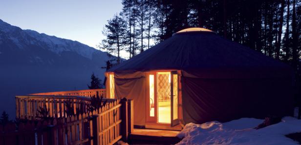 Eine Jurte mit beleuchtetem Eingang vor einer Bergkulisse in der Dämmerung.