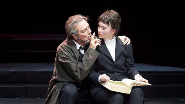 Ein Mann flüstert einer jungen Frau mit einem Buch etwas ins Ohr.