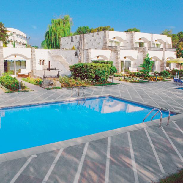 Ein Schwimmbad vor einem Hotel mit weißer Fassade an einem sonnigen Tag.