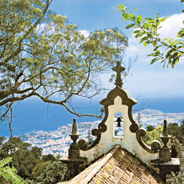 Blick auf eine Glocke in einem alten Glockenturm mit einer Stadt im Hintergrund.