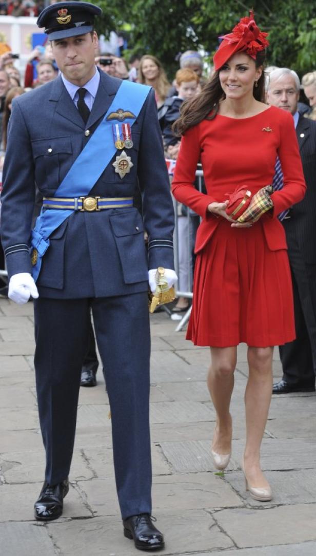 Prinz William in Uniform und Kate Middleton in einem roten Kleid gehen zusammen.