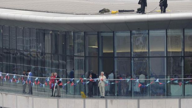 Menschen stehen auf einem Balkon mit blau-weiß-roter Dekoration.
