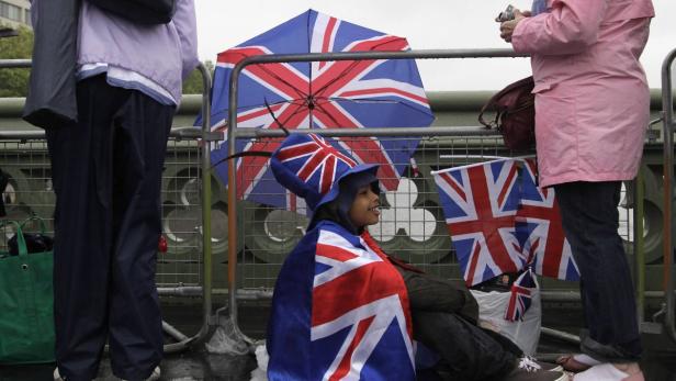 Eine junge Person mit Union-Jack-Hut und -Flagge wartet an einer Absperrung.