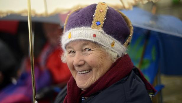 Eine lächelnde ältere Frau mit einer gestrickten Krone auf dem Kopf.