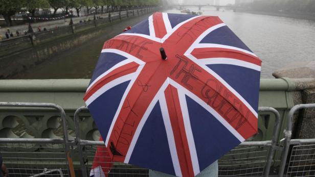 Ein Regenschirm mit dem Union Jack und der Aufschrift „Save the Queen“ vor einem Fluss.