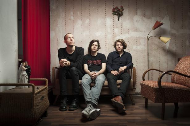 Drei Männer sitzen auf einem Sofa vor einer floralen Tapete.