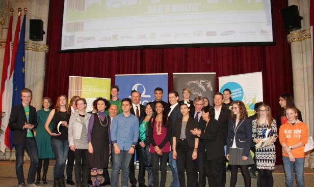 Eine Gruppe von Menschen steht auf einer Bühne vor einem roten Vorhang.