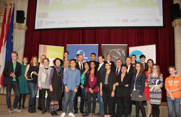 Eine Gruppe von Menschen steht auf einer Bühne vor einem roten Vorhang.