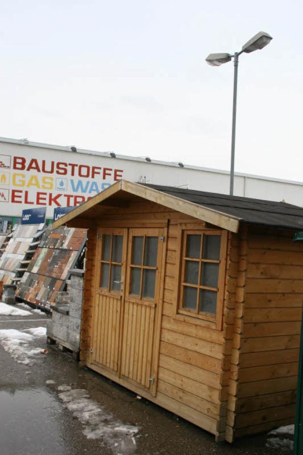 Ein kleines Holzhaus steht vor einem Baumarkt.