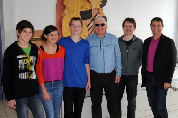 Eine Gruppe von sechs Personen posiert für ein Foto vor einer Wanddekoration.