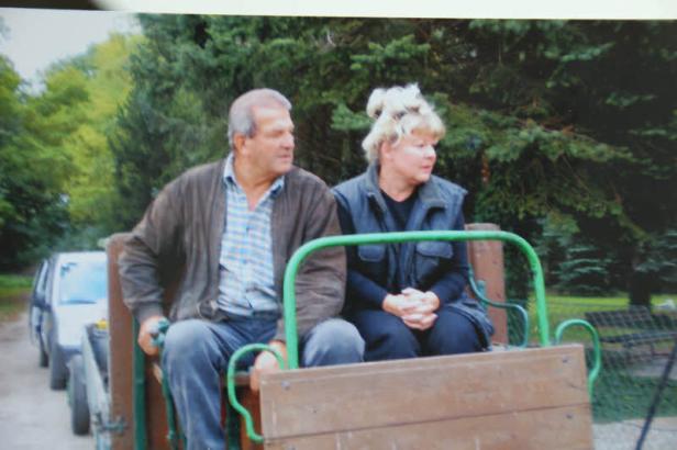 Ein älteres Paar sitzt in einem Wagen, der von einem Auto gezogen wird.