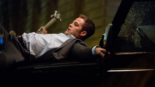 Ein Mann liegt auf der Motorhaube eines Autos und hält einen Hammer in der Hand.