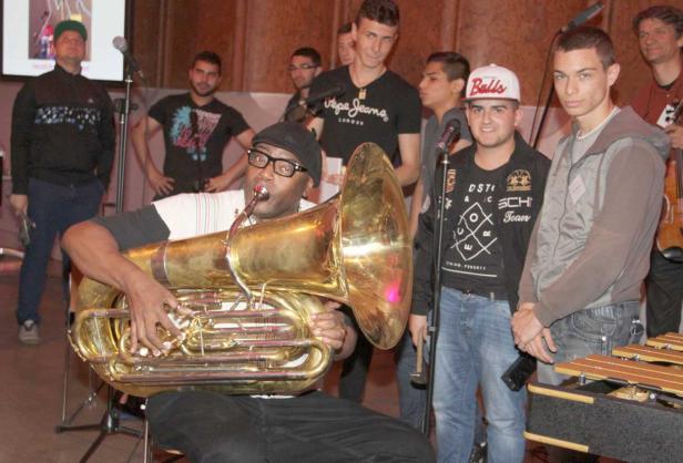 Ein Mann mit Brille spielt Tuba vor einer Gruppe von Menschen.