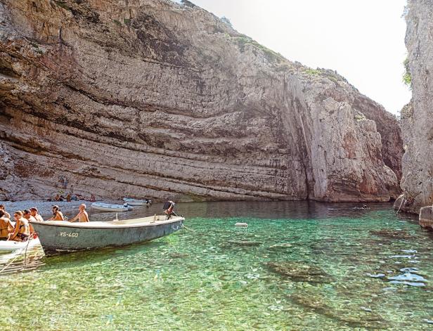 Ein Boot liegt in einer Bucht mit kristallklarem Wasser und hohen Felswänden.