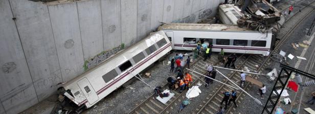 Ein entgleister Zug liegt neben einer Betonmauer, Rettungskräfte sind vor Ort.