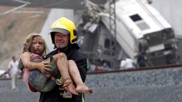 A fireman carries an injured child from the wrecka Ein Feuerwehrmann trägt ein schmutziges, verletztes Mädchen vor einem entgleisten Zug weg.