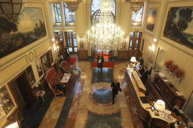 … Die Lobby eines Hotels mit Marmorboden, einem großen Kronleuchter und mehreren Gästen.