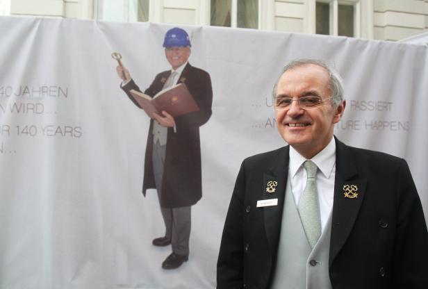… M. Moser posiert vor einem Banner mit einem Bild von ihm mit Bauhelm und Schlüssel.