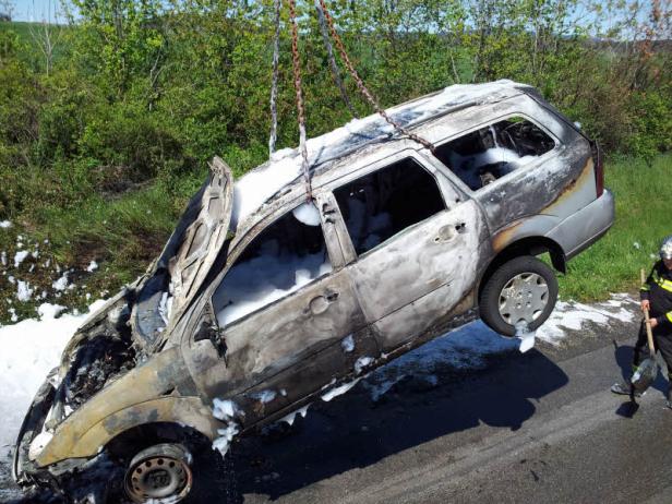 Ein ausgebranntes Auto wird mit einer Kette von der Straße gehoben.