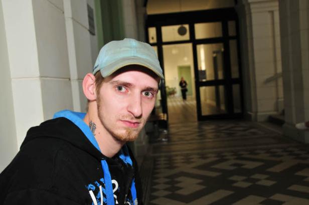 Ein Mann mit Bart und Kappe steht vor einem Gebäude.