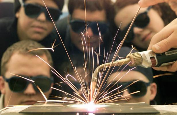 Eine Gruppe von Personen mit Schutzbrillen beobachtet das Schweißen.