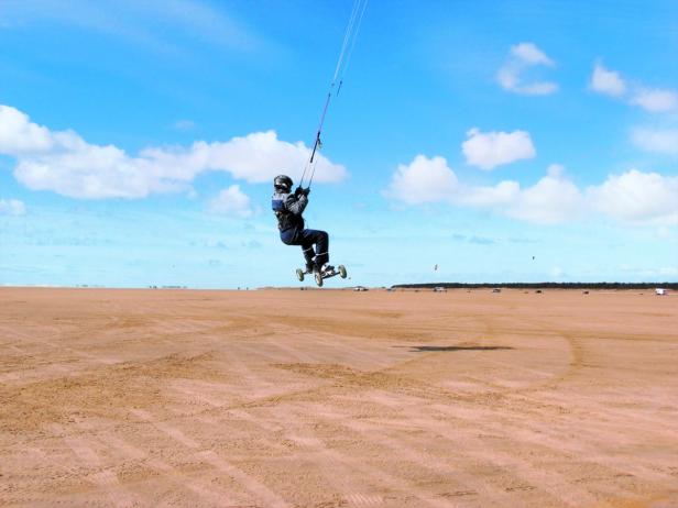 Ein Kitesurfer fährt mit einem Kitebuggy über einen Sandstrand.