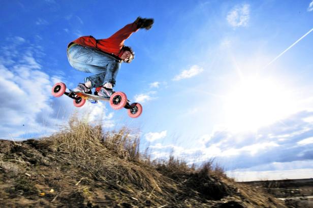 Ein Mann springt mit einem Mountainboard über einen Hügel.