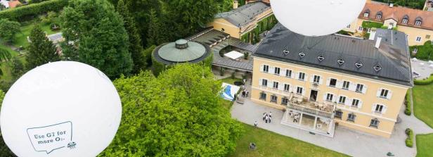 Luftaufnahme eines gelben Schlosses mit grüner Umgebung und weißen Ballons.