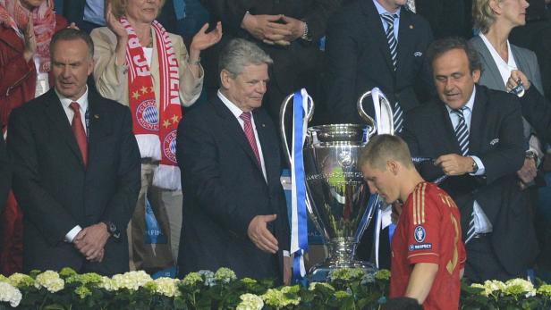 Bastian Schweinsteiger mit der Champions-League-Trophäe und mehreren Anzugträgern im Hintergrund.