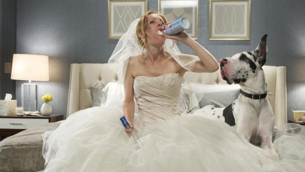 Eine Braut im Hochzeitskleid isst Schlagsahne direkt aus der Dose, neben ihr eine Dogge.