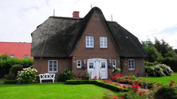 Ein reetgedecktes Backsteinhaus mit einem gepflegten Garten voller Blumen.