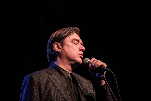 David Byrne singt mit geschlossenen Augen in ein Mikrofon.