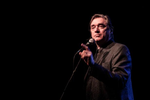 Ein Mann mit Anzug steht auf einer Bühne und spricht in ein Mikrofon.