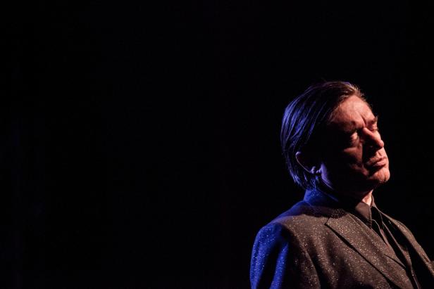 Ein Mann im Anzug steht mit geschlossenen Augen im Dunkeln.