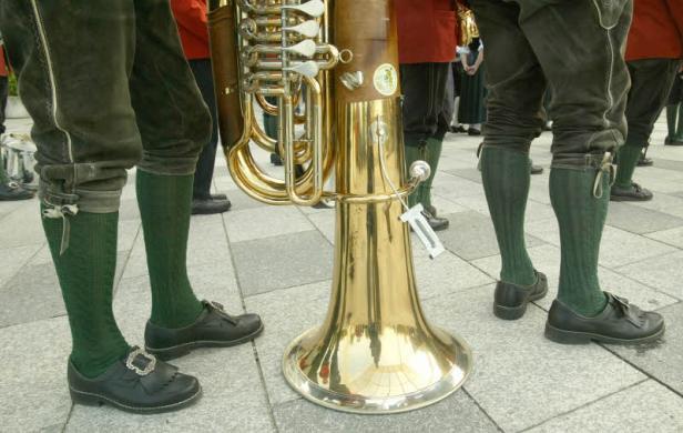 Eine Tuba steht vor Musikern in Tracht mit grünen Kniestrümpfen und Lederschuhen.