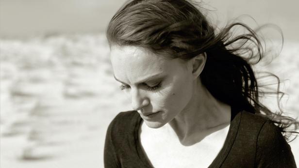 Schwarzweißaufnahme von Natalie Portman, die nach unten blickt, während ihr Haar im Wind weht.