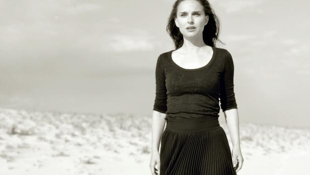 Natalie Portman steht in einem schwarzen Kleid in einer wüstenähnlichen Landschaft.