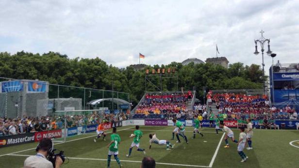 Ein Fußballspiel mit Zuschauern im Hintergrund, im Zentrum Berlin mit Reichstag und Deutschlandflagge.