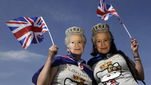 Zwei Frauen mit Queen-Elizabeth-Masken und Union-Jack-Flaggen feiern.