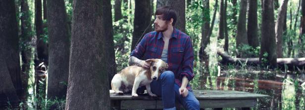 Ein Mann sitzt mit seinem Hund auf einer Bank in einem Waldgebiet.