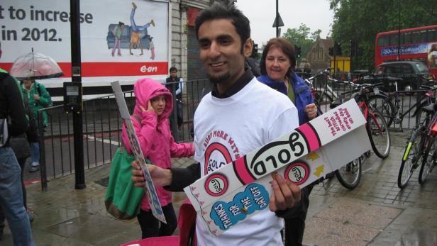 Ein Mann mit einem „Gold“-Werbeschild steht auf einer belebten Straße.