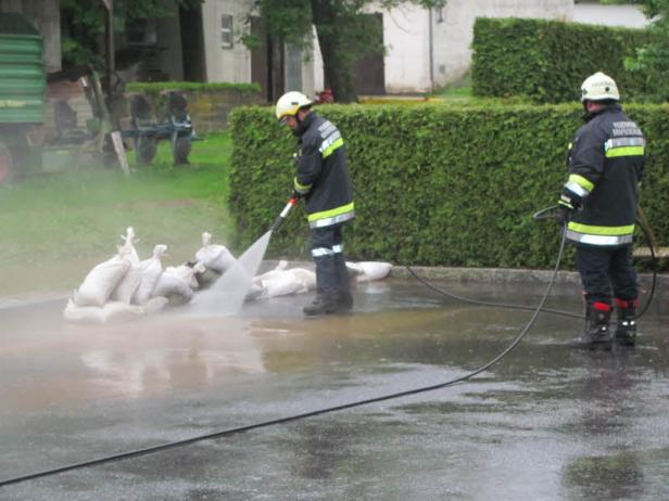 Zwei Feuerwehrleute reinigen Sandsäcke mit einem Hochdruckreiniger.