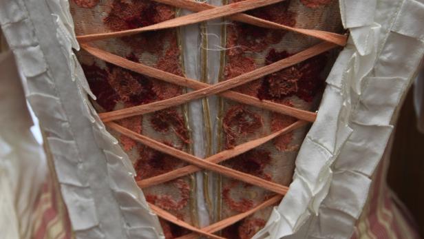 Die Rückseite eines historischen Kleides mit Schnürung und Rüschen.