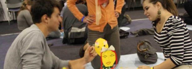 Zwei junge Leute sitzen auf dem Boden und basteln an gelben Masken.