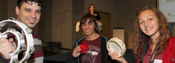 Drei lächelnde Personen halten Musikinstrumente in die Kamera.