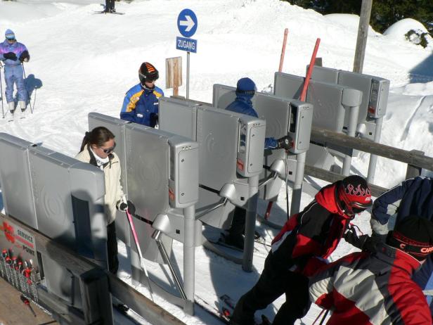 Skifahrer passieren ein Drehkreuz an einem verschneiten Hang.