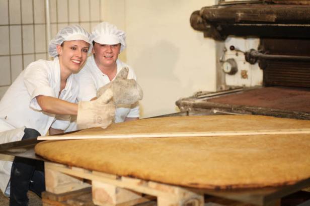 Zwei Bäckerinnen präsentieren ein riesiges Gebäckstück in einer Bäckerei.