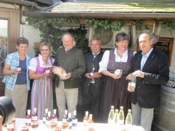 Eine Gruppe von Menschen in Tracht präsentiert regionale Produkte wie Marmelade und Wein.