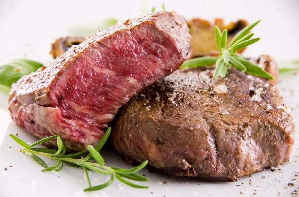 Zwei saftige Steaks, garniert mit Rosmarin und Gewürzen, liegen auf einem Teller.