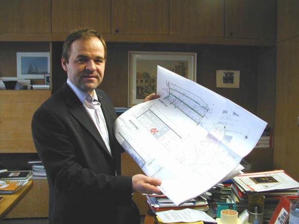 Ein Mann im Anzug präsentiert einen Bauplan in einem Büro.